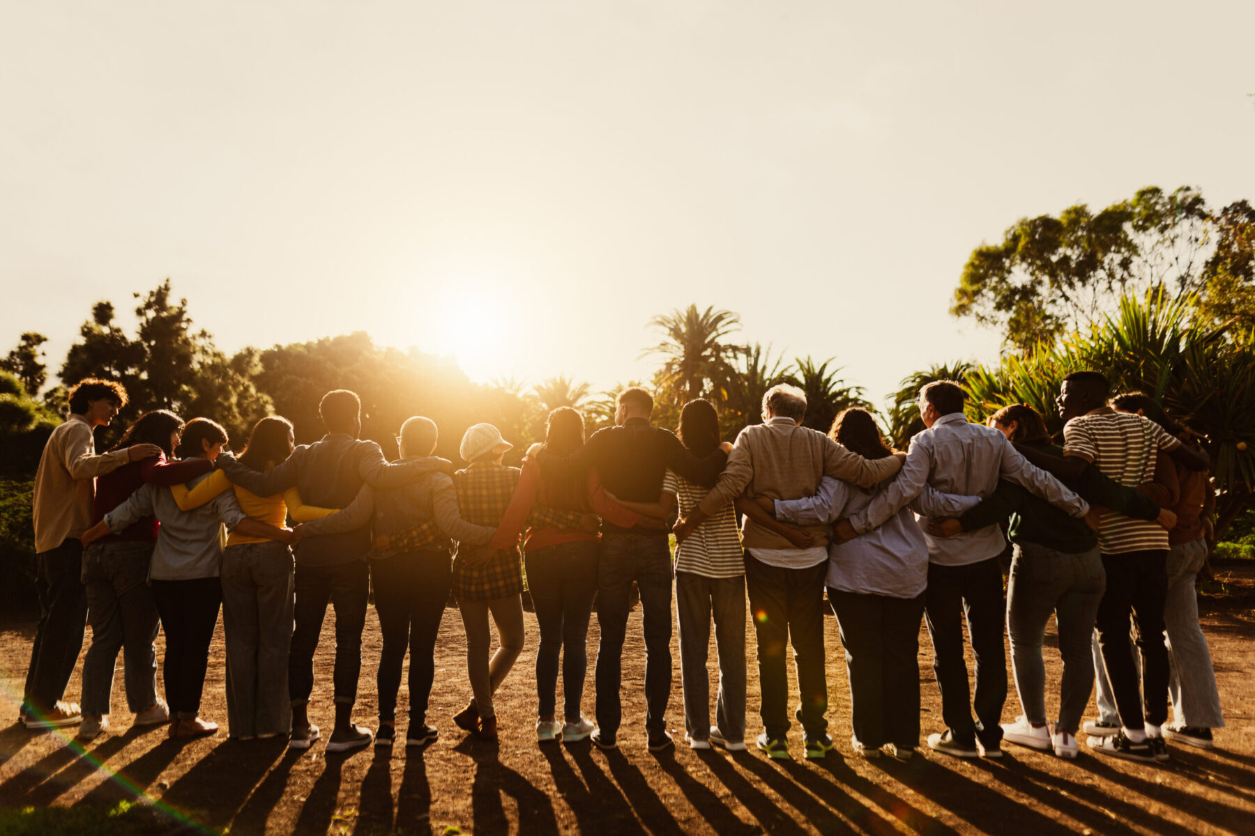 Large group of people with arms together at sunset.